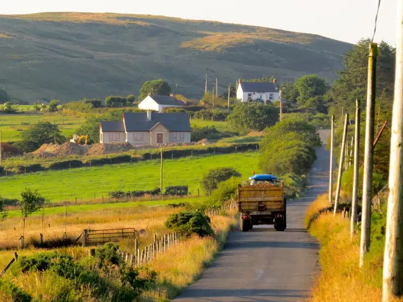 tractor in a narrow lane in Northern Ireland, surrounded by hedgerows and small houses in the distance