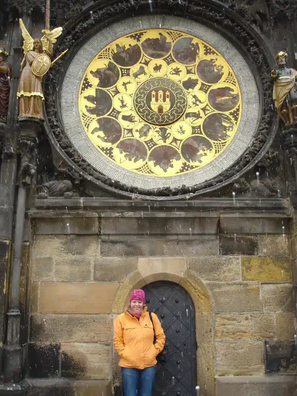 Part of the astronomical closk in Prague with a woman in an orane coat and pink hat standing underneath